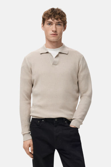 Pull col V beige de MANGO, porté avec un t-shirt blanc et un jean noir.