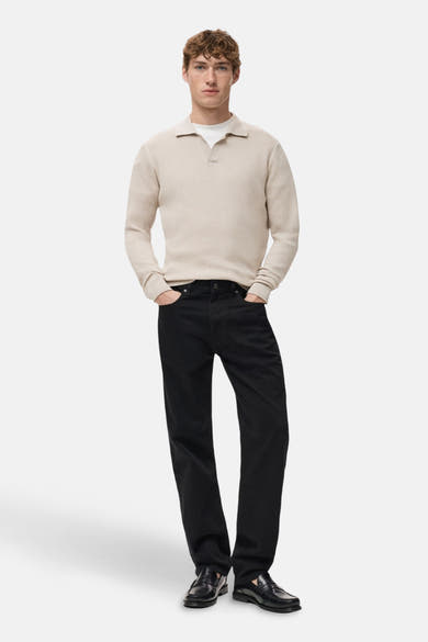 Pull à col en V beige de MANGO, porté avec un t-shirt blanc, un jean noir et des mocassins noirs.