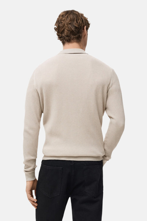 Pull col V beige de MANGO, en maille côtelée, porté avec un pantalon noir.