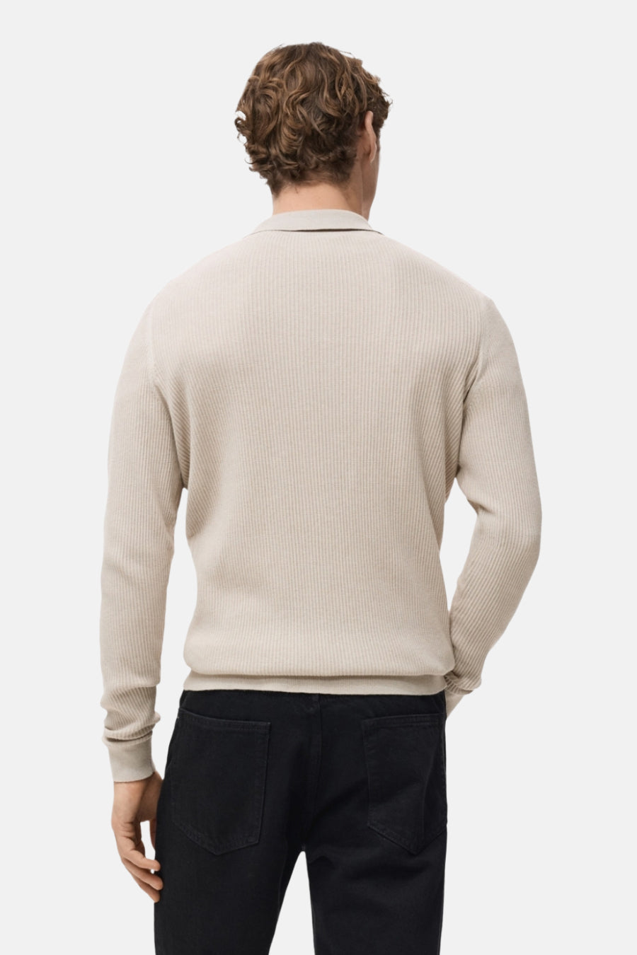 Pull col V beige de MANGO, en maille côtelée, porté avec un pantalon noir.