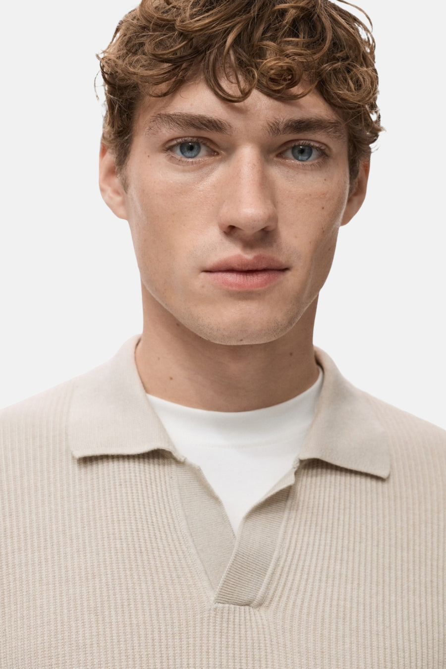 Pull à col en V beige de MANGO, en maille côtelée, porté avec un t-shirt blanc uni.
