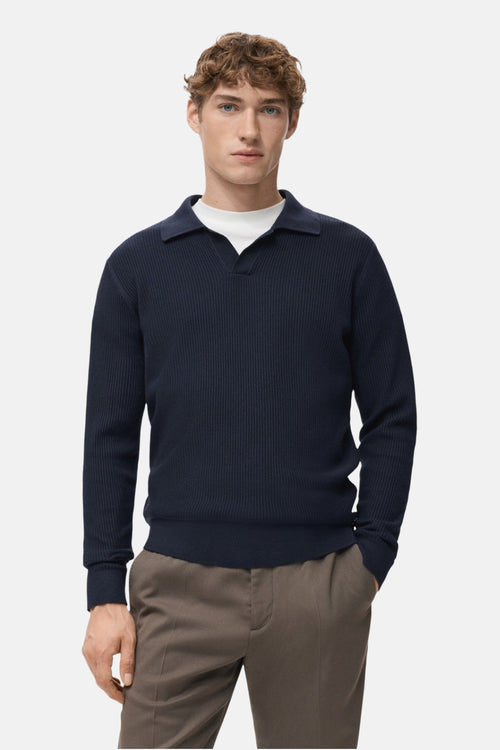 Pull à col en V bleu de MANGO, en maille côtelée, porté avec un t-shirt blanc et un pantalon marron.
