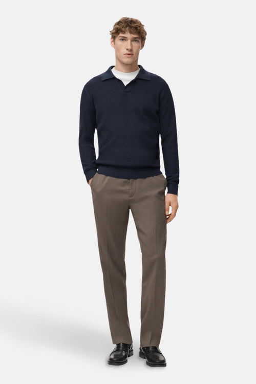 Pull à col en V bleu par MANGO, porté sur un t-shirt blanc, avec un pantalon marron clair et des chaussures noires.