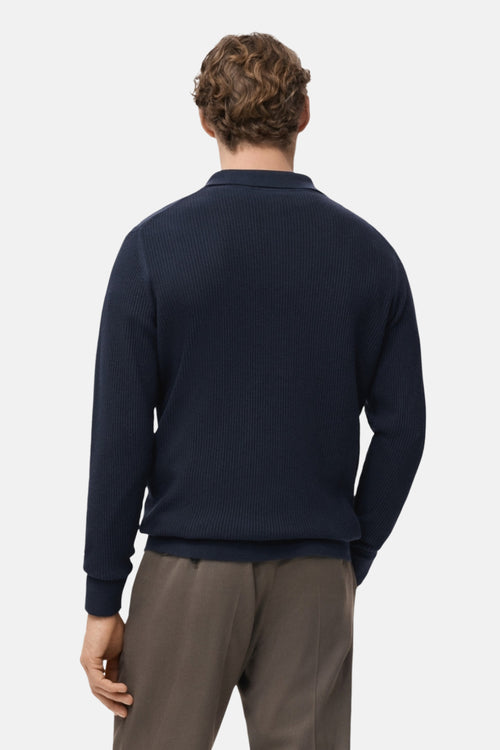 Pull à col en V bleu de MANGO, texture côtelée, porté avec un pantalon décontracté marron, vue de dos.
