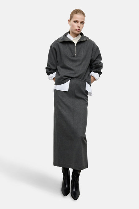 Grijze sweatshirt met ritssluiting van MANGO, gedragen over een wit overhemd, met een bijpassende lange rok en zwarte enkellaarsjes.
