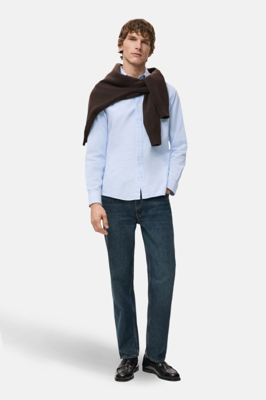 Blauw overhemd met lange mouwen van MANGO, gedragen met een bruine trui over de schouders, met een spijkerbroek en zwarte schoenen.