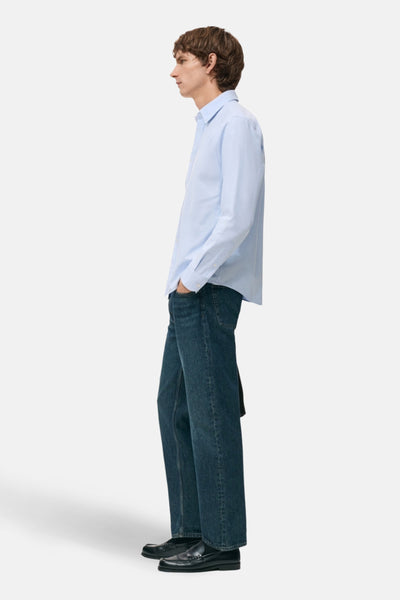 Lichtblauw overhemd met lange mouwen van MANGO, gedragen met een donkere spijkerbroek en zwarte loafers, van opzij gezien.