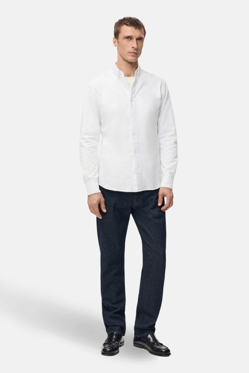Chemise blanche à manches longues de MANGO, portée avec un jean bleu foncé et des mocassins noirs.