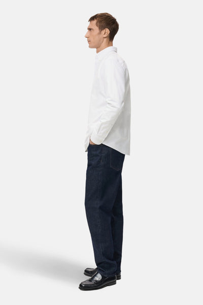 Wit overhemd met lange mouwen van MANGO, gedragen met een donkerblauwe jeans en zwarte loafers, zijwaarts gezien.