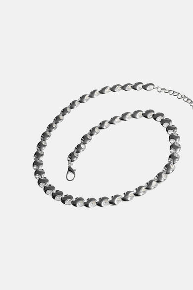 Collier court argenté de MANGO, orné de pierres brillantes, sur fond uni.
