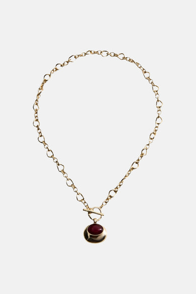 Collier court doré par MANGO, avec un pendentif rond bordeaux et une chaîne à maillons originaux.

