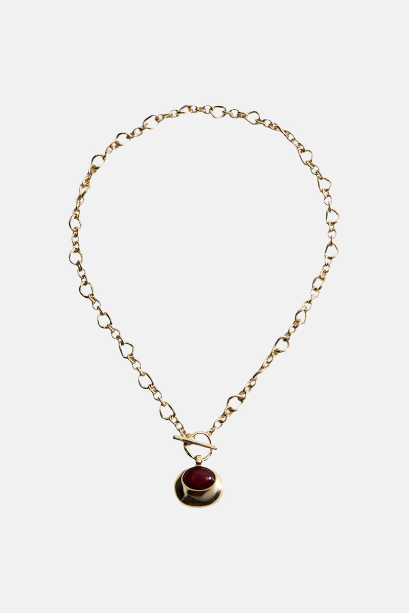 Collier court doré par MANGO, avec un pendentif rond bordeaux et une chaîne à maillons originaux.
