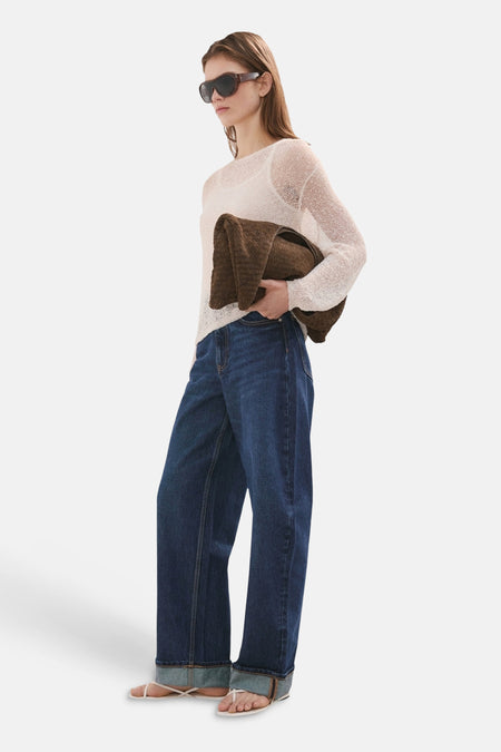 Jean denim bleu foncé de MANGO, porté avec un pull beige et des sandales à lanières.
