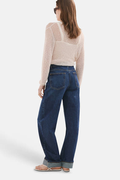 Jean en denim bleu foncé de MANGO, porté avec un haut en maille ajourée et des sandales.