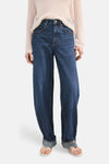Jean en denim bleu foncé de MANGO, avec une coupe ample et des ourlets roulés, porté avec un pull beige.
