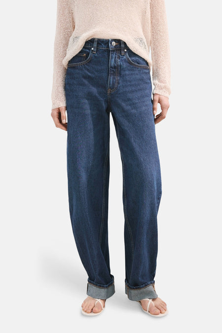 Jean en denim bleu foncé de MANGO, avec une coupe ample et des ourlets roulés, porté avec un pull beige.
