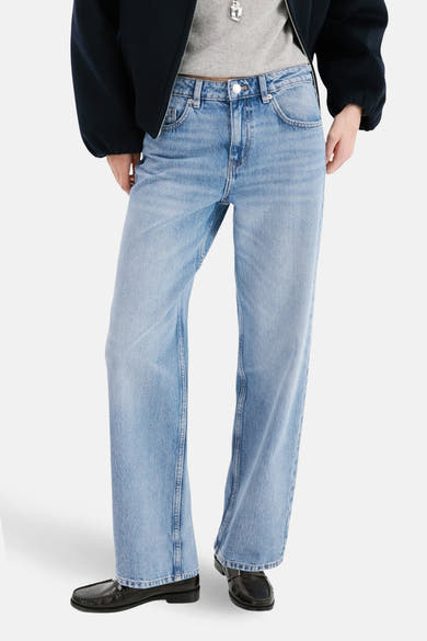Jean droit en denim bleu clair de MANGO, porté avec un t-shirt gris, une veste bleu marine et des mocassins noirs.
