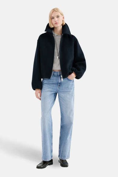 Jean droit en denim bleu clair de MANGO, porté avec un blouson noir, un polo gris et des mocassins noirs.
