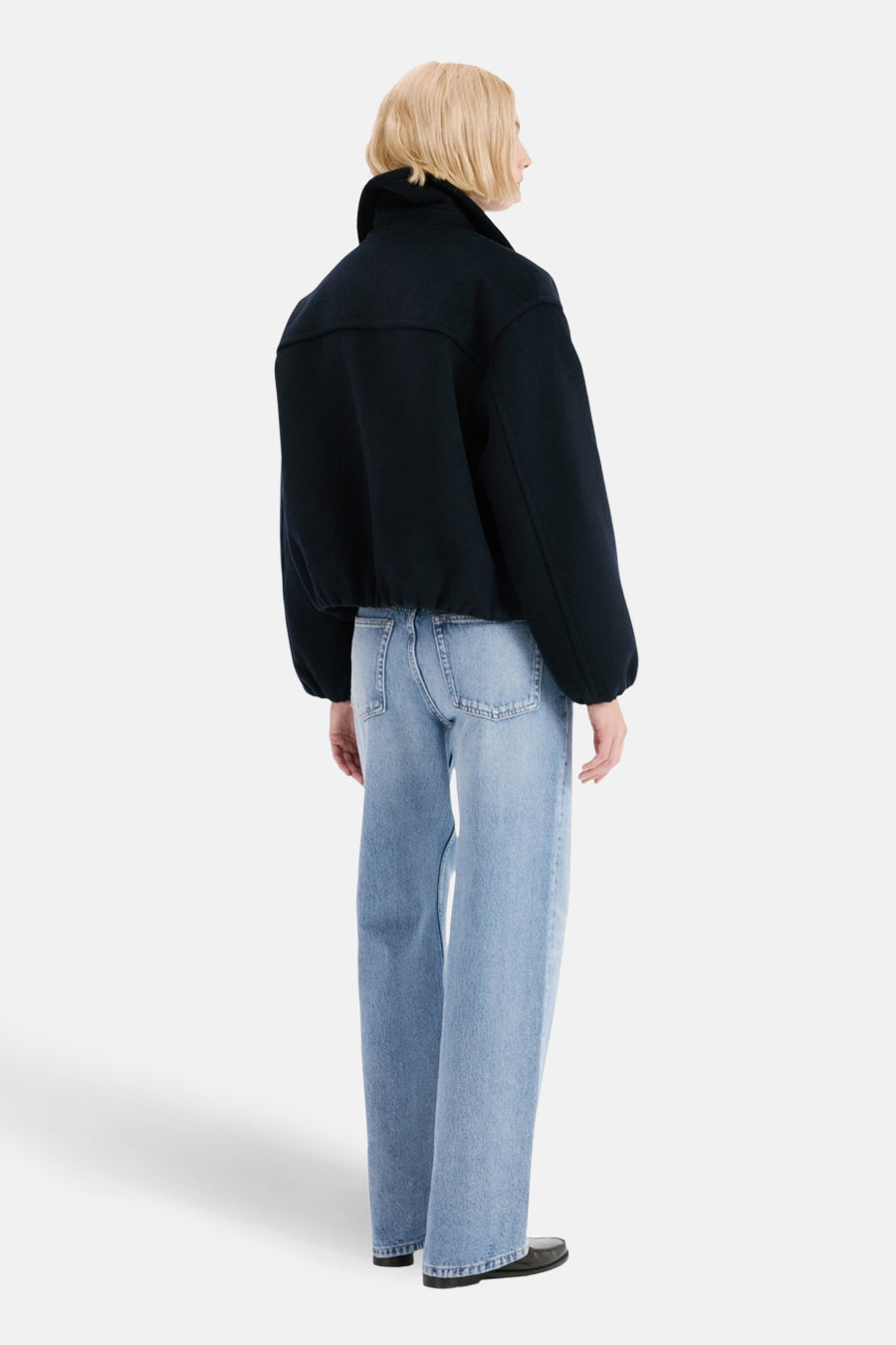 Jean droit en denim bleu clair de MANGO, porté avec une veste courte noire et des chaussures noires.