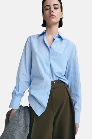 Chemisier bleu à rayures, de MANGO, porté avec un pantalon vert olive et une ceinture noire.