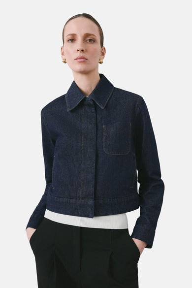 Veste en jean bleu foncé de MANGO, avec poche poitrine et portée sur un haut blanc et un pantalon noir.