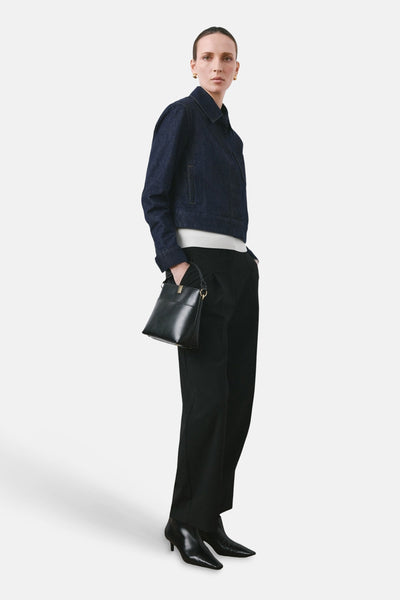 Veste en jean en denim bleu foncé de MANGO, portée avec un pull blanc, un pantalon noir et des bottines.