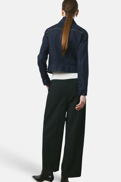 Veste en jean bleu foncé de MANGO, vue de dos, portée avec un pull blanc et un pantalon noir large.
