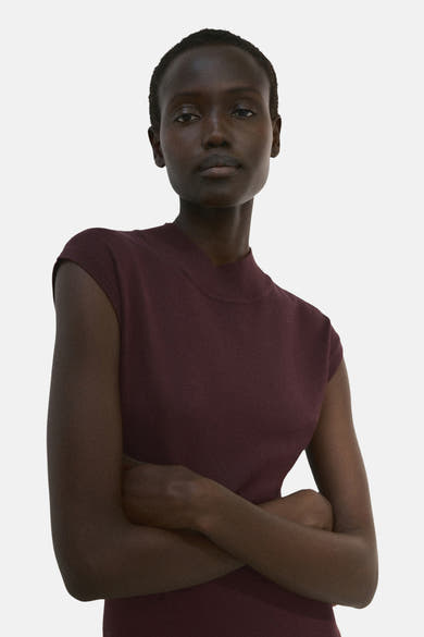 Robe à manches courtes brune de MANGO, portée par une femme aux bras croisés.