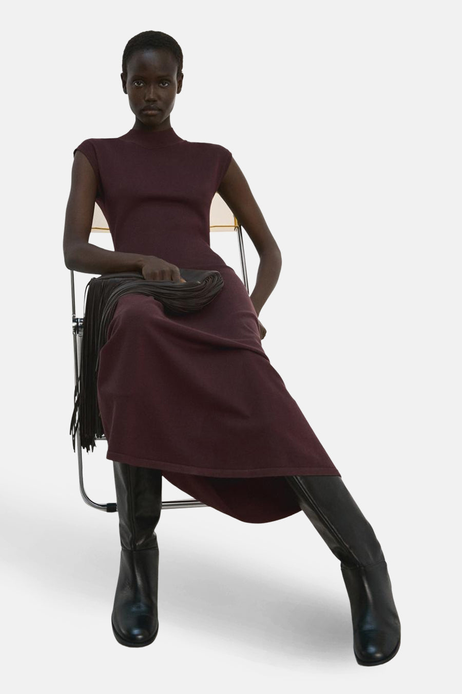 Robe à manches courtes marron de MANGO, portée avec des bottes en cuir noir et une pochette à franges.