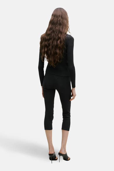 Gilet noir de MANGO, porté avec un pantalon noir et des mules à talons hauts, vue arrière.
