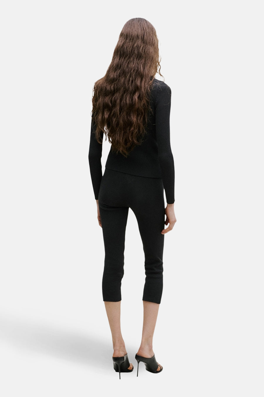 Gilet noir de MANGO, porté avec un pantalon noir et des mules à talons hauts, vue arrière.
