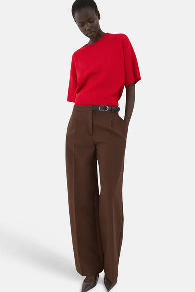 Pull col rond rouge de MANGO, porté avec un pantalon marron taille haute et une ceinture noire.
