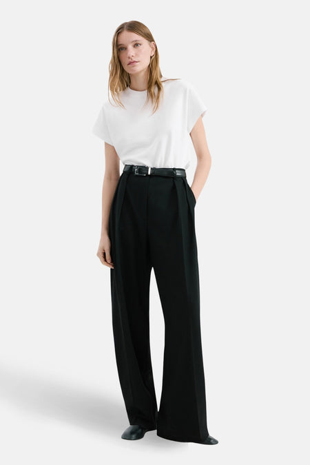 Chemisier blanc à manches longues par MANGO, porté avec un pantalon taille haute noir et une ceinture.