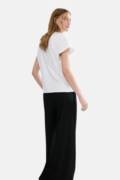 Wit overhemd met lange mouwen van MANGO, gedragen met een wijde zwarte broek, van achteren gezien.