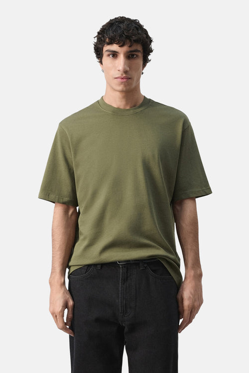 T-shirt à manches courtes kaki de MANGO, porté avec un jean noir, sur fond blanc.