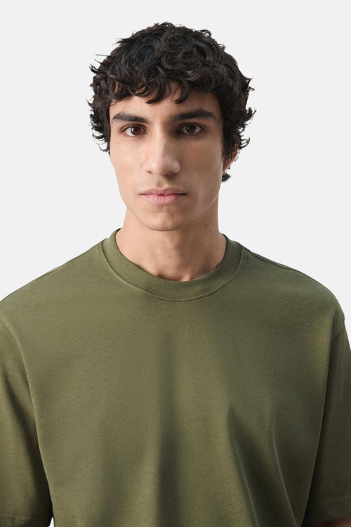 T-shirt kaki à manches courtes de MANGO, uni, porté par un homme aux cheveux bruns frisés.

