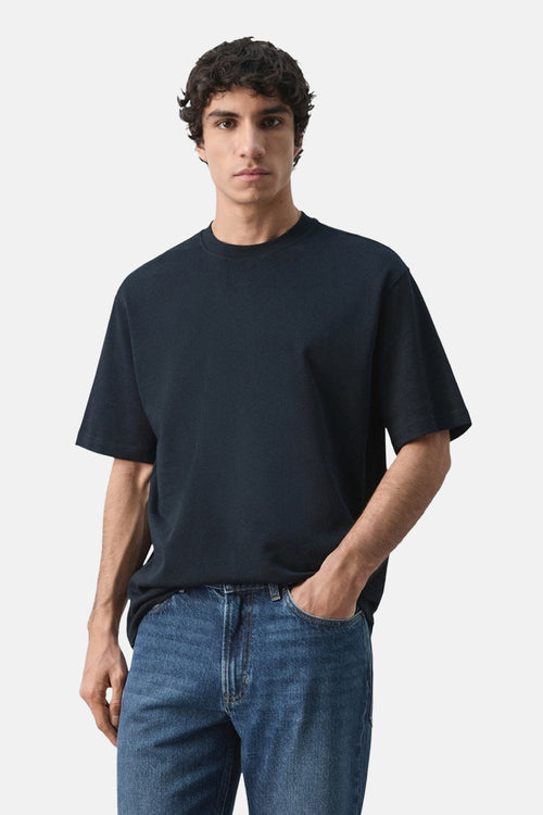 T-shirt bleu à manches courtes de MANGO, porté avec un jean bleu et une main dans la poche.