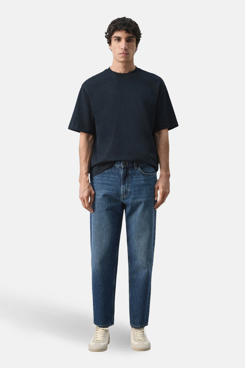 T-shirt à manches courtes bleu de MANGO, porté avec un jean bleu décontracté et des chaussures de sport couleur crème.