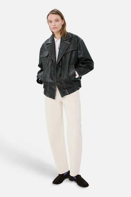 Jean blanc en denim de MANGO, porté avec une veste en cuir noir et des mocassins.
