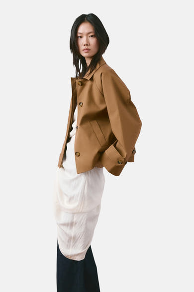 Kort bruin jasje van MANGO, gedragen over een witte jurk, gecombineerd met een donkere broek.