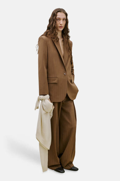 Pantalon de costume brun par MANGO, ample avec rayures verticales fines, porté avec un blazer assorti et un foulard clair noué.