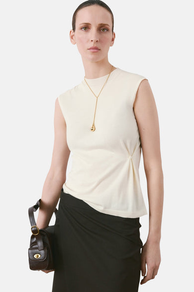 Top beige sans manches de MANGO, porté avec un collier doré et une jupe noire.