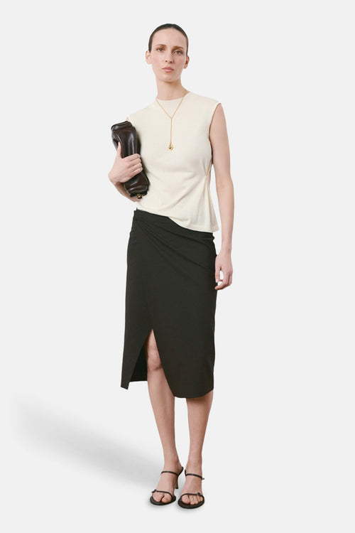 Beige mouwloze top van MANGO, gedragen met een zwarte wikkelrok en sandalen met bandjes.