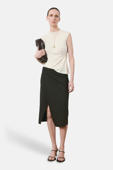 Top sans manches beige de MANGO, porté avec une jupe portefeuille noire et des sandales à brides.