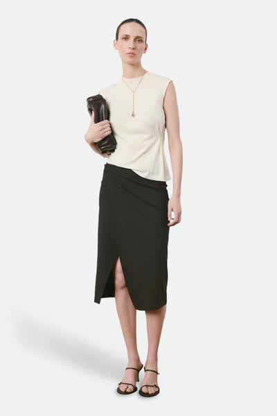 Top sans manches beige de MANGO, porté avec une jupe portefeuille noire et des sandales à brides.