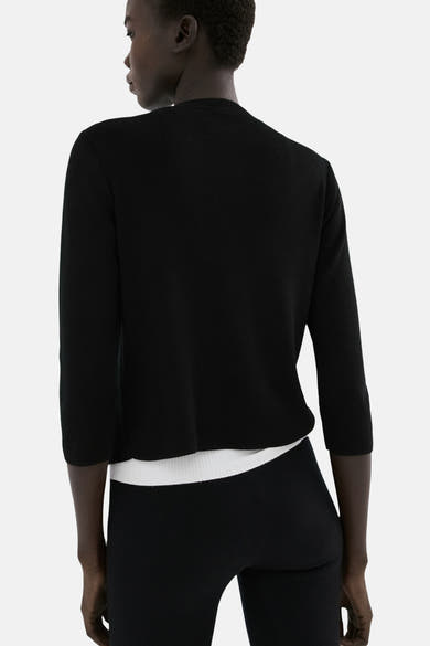 Gilet noir de MANGO, en maille fine avec manches trois-quarts, porté sur un haut blanc et un pantalon noir.