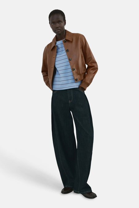 T-shirt bleu rayé de MANGO, porté avec une veste en cuir marron et un pantalon ample.
