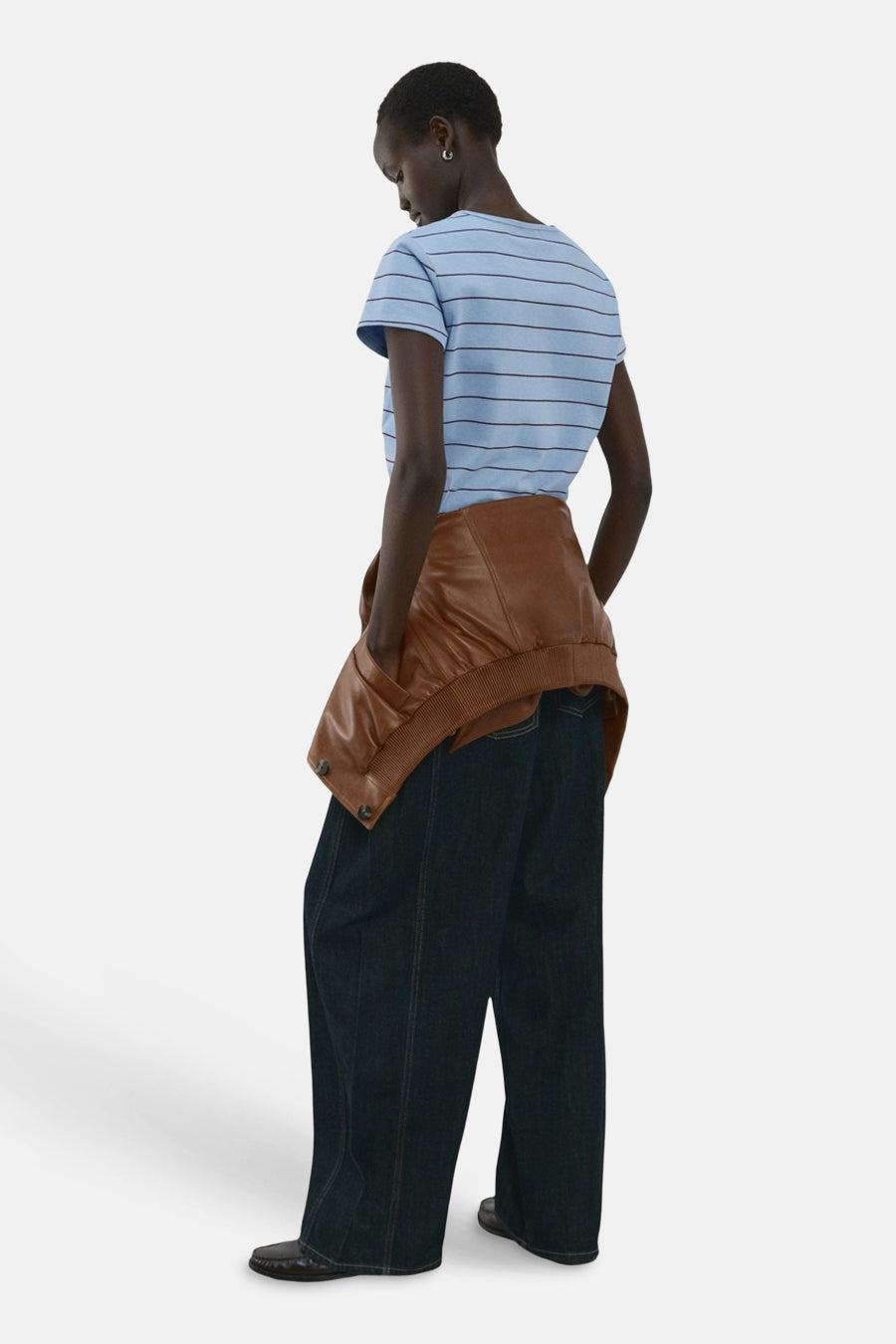 T-shirt bleu rayé de MANGO, porté avec une veste en cuir marron nouée à la taille et un pantalon ample bleu foncé.