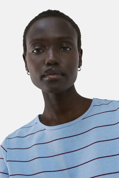 Blauw T-shirt met bordeauxrode strepen van MANGO, gedragen door een vrouw met een donkere huid en zilveren oorbellen.