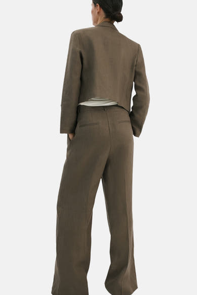 Pantalon kaki par MANGO, coupe ample, avec des poches arrière passepoilées, et porté avec une veste courte marron.
